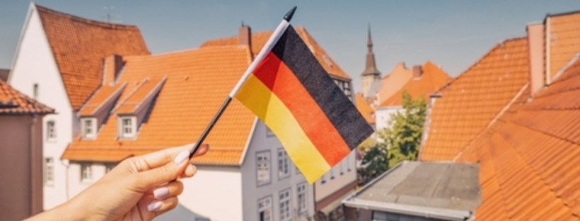 A hand holding a small German flag above the orange roofs of a German town, illustrative photo for the exit tax post