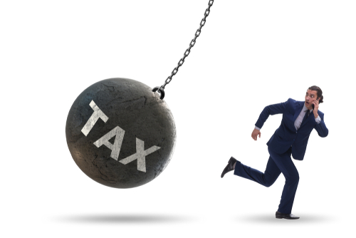 An illustration of a wrecking ball labeled TAX swinging after a businessman running away, illustrating the article on moving to Germany with a U.S. trust