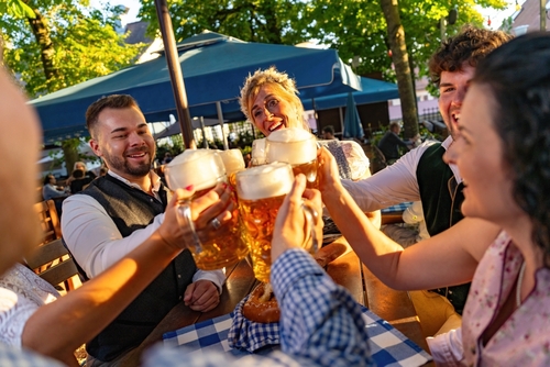 A group of friends raising and clinking large beer steins at an outdoor German beer garden, illustrating the article on a U.S. trust with a beneficiary in Germany