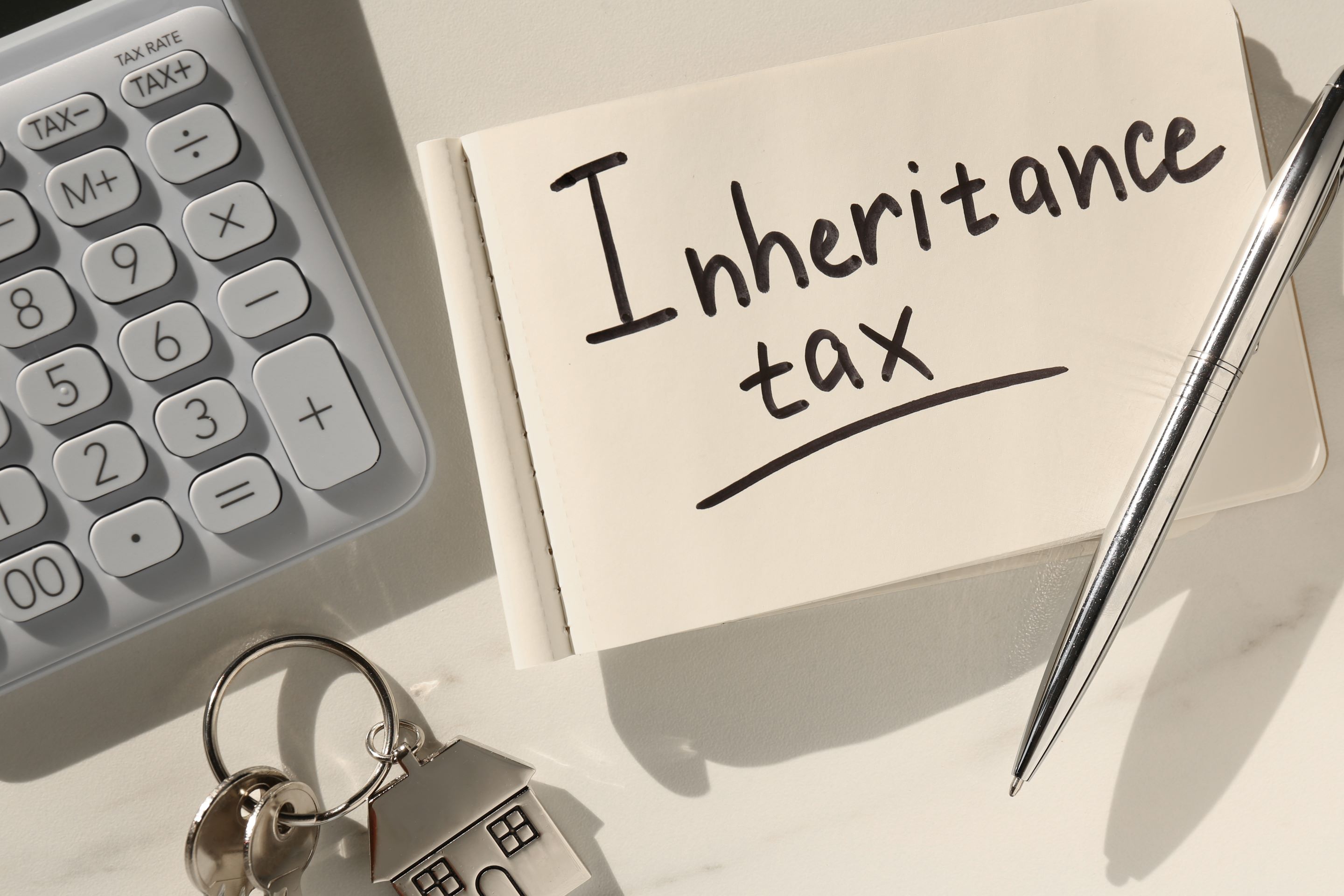 A notebook reading Inheritance tax beside a calculator, a pen, and a house-shaped keyring, illustrating the article on a German resident inheriting from the United States
